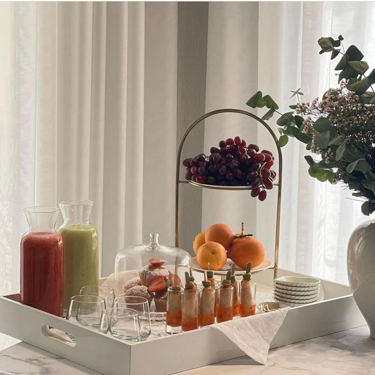 a tray filled with fruit and drinks on top of a table next to a vase