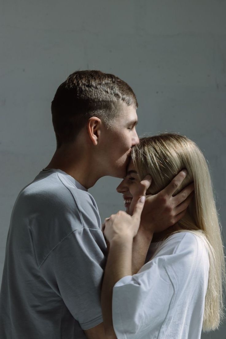 a man and woman kissing each other in front of a white wall with their arms around one another