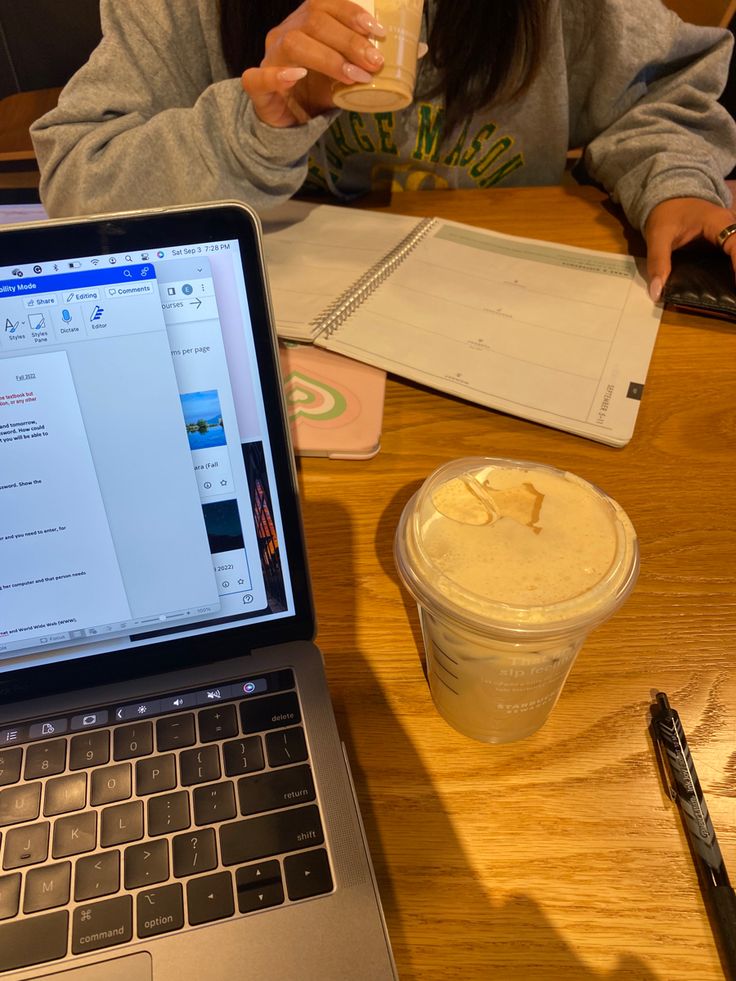 a person sitting at a table with a laptop and a drink in front of them