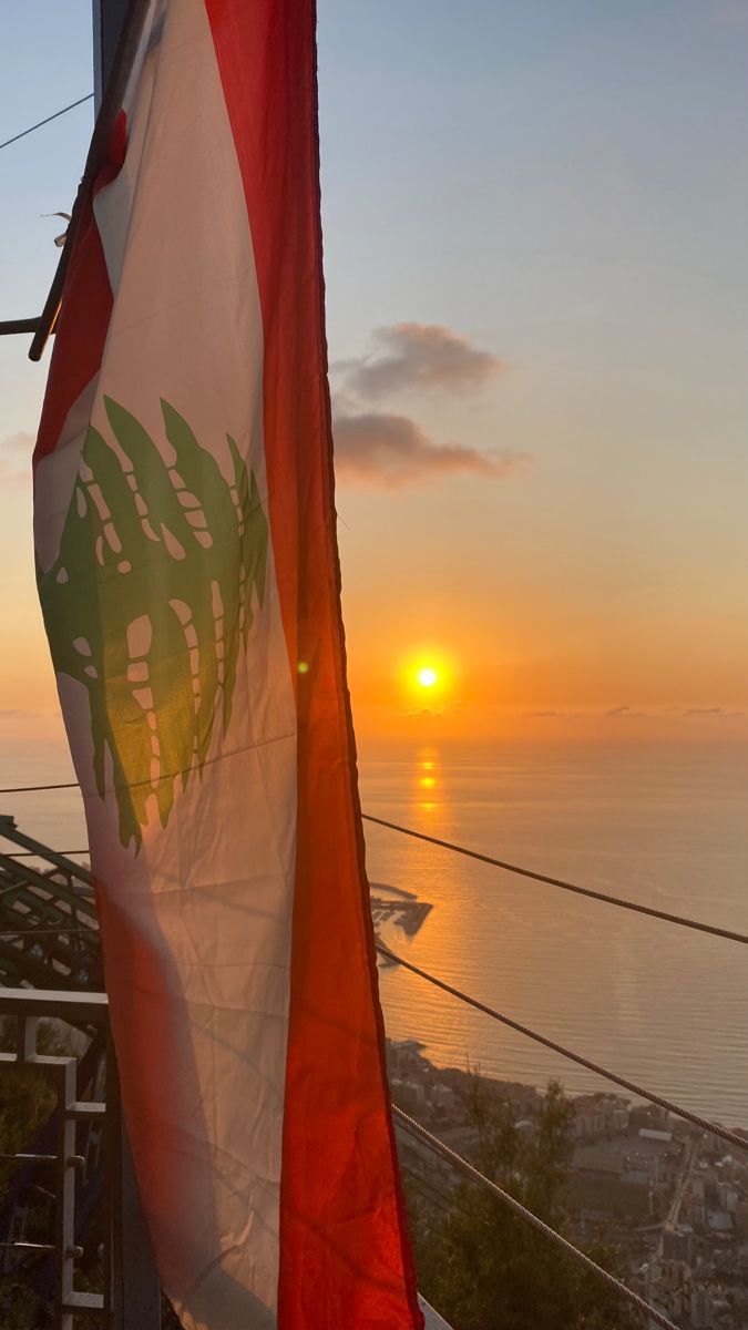 the sun is setting behind a flag on top of a building with water in the background