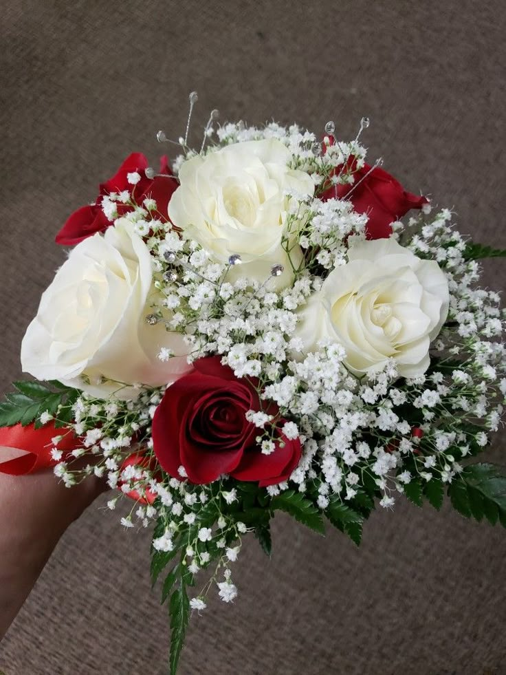 a bouquet of white and red roses with baby's breath in someones hand