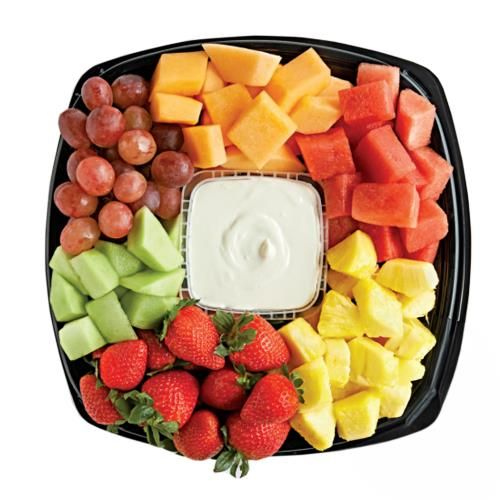 a platter filled with fruit and dip surrounded by grapes, strawberries, melon, pineapples, kiwis