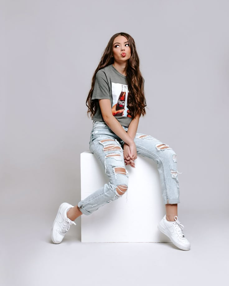 a young woman sitting on top of a white block wearing ripped jeans and a coca cola t - shirt