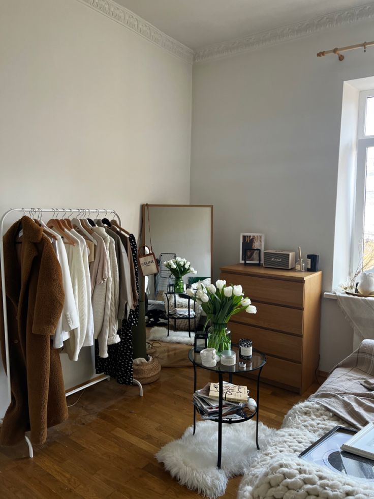 a room filled with lots of clothes on hangers next to a dresser and window