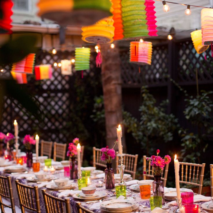 a long table is set with colorful paper lanterns and place settings for an outdoor dinner