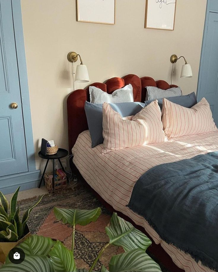 a bed with blue and pink pillows in a bedroom next to two green planters