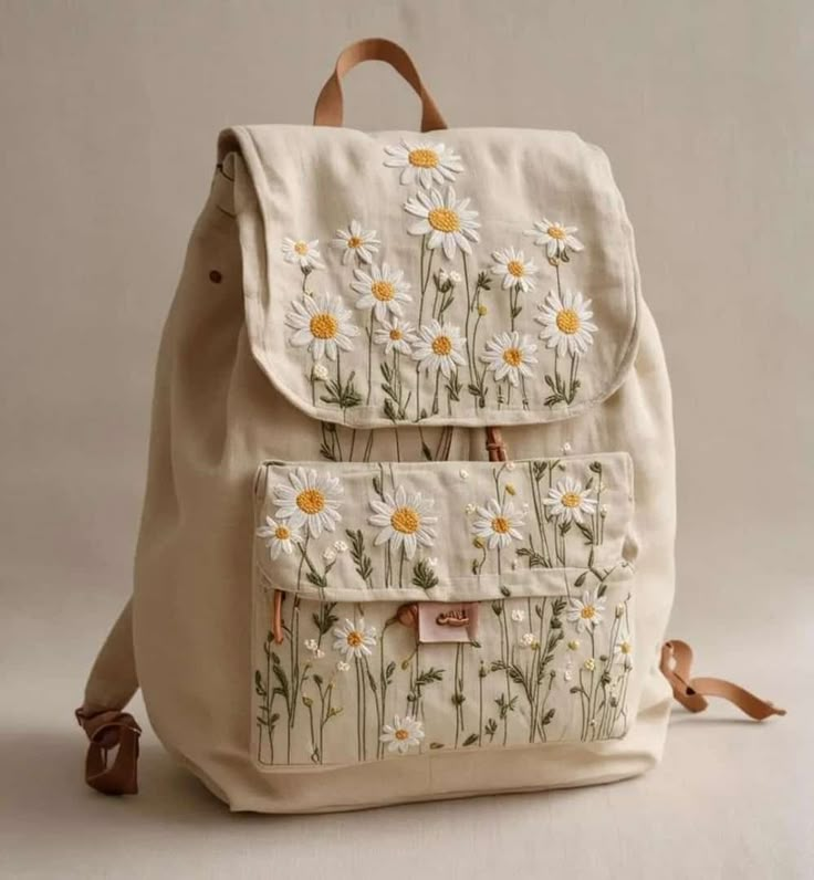 a white backpack with daisies on the front and back straps, sitting against a white background