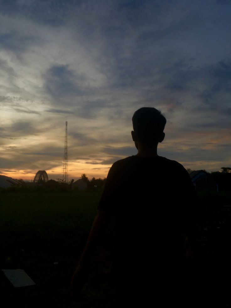 the silhouette of a man standing in front of a dark sky with clouds above him