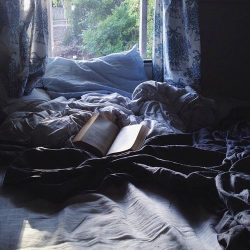 an open book laying on top of a bed in front of a window with curtains