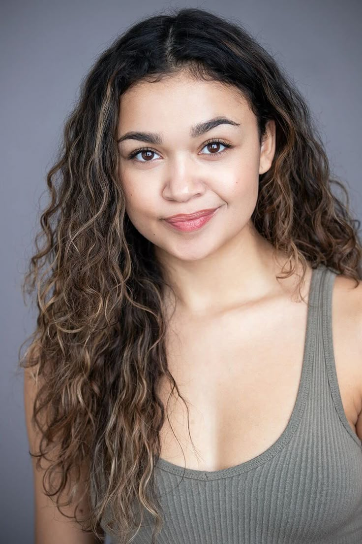 a beautiful young woman with long curly hair posing for a photo in front of a gray background