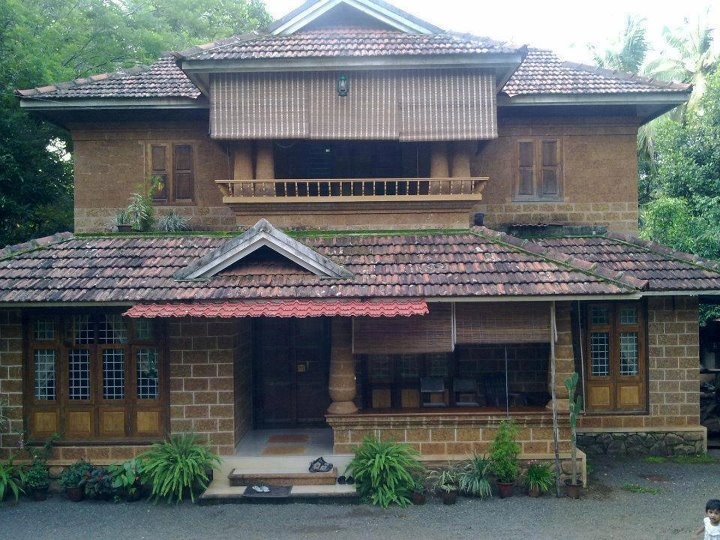 an old style house in the middle of some trees and bushes with a little boy walking by it