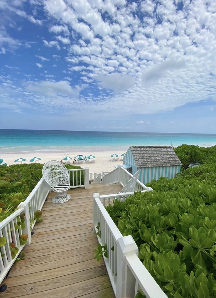 a wooden walkway leading to the beach with umbrellas and chairs on it's sides