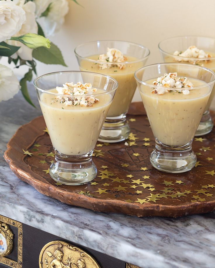 four glasses filled with dessert sitting on top of a wooden tray next to white flowers