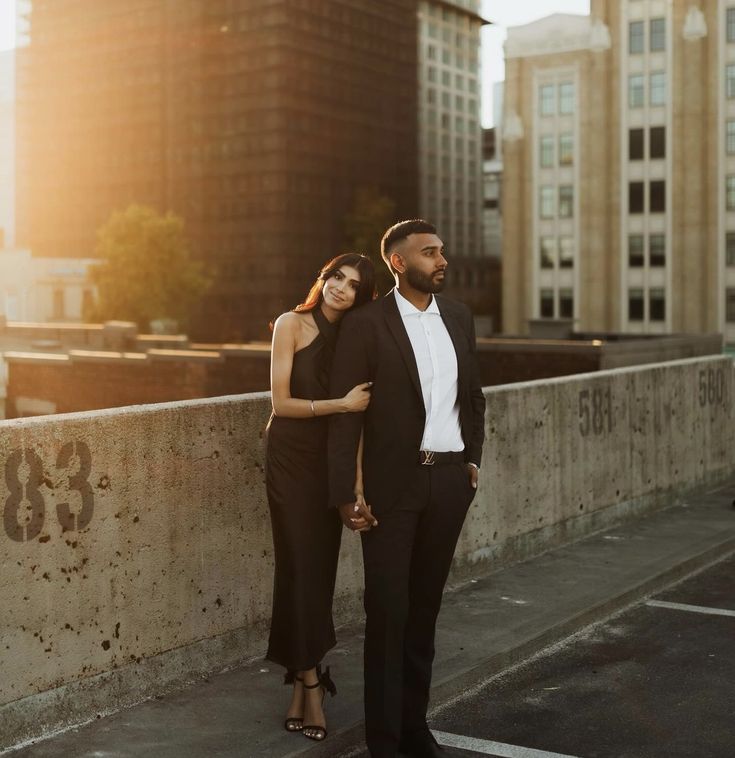 a man and woman standing next to each other on top of a bridge in front of tall buildings