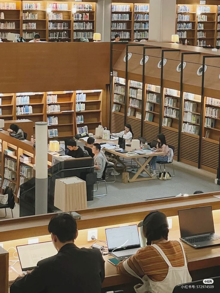 people sitting at tables in a library with laptops and bookshelves full of books