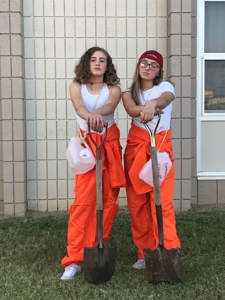 two girls in orange pants are holding shovels and standing next to each other on the grass