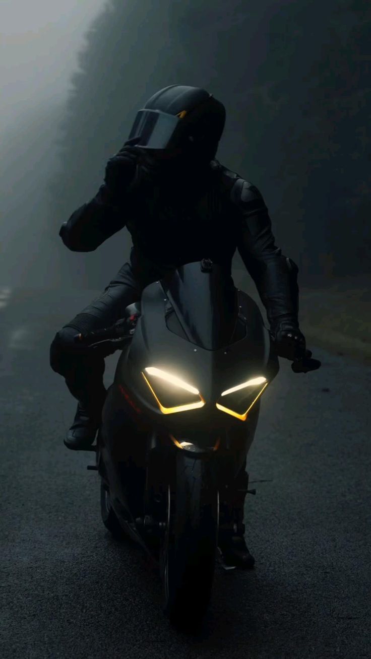 a man riding on the back of a motorcycle down a foggy road at night