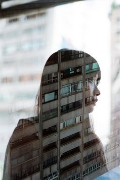 a woman's face is reflected in the window of a building with multiple balconies