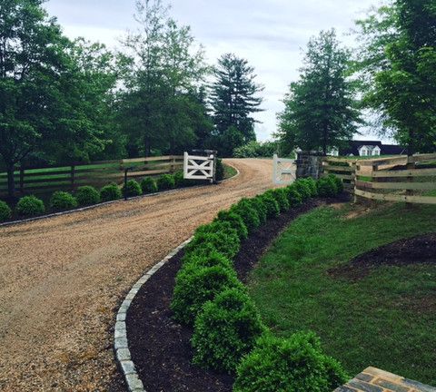 a dirt road surrounded by green trees and bushes with a white gate in the middle