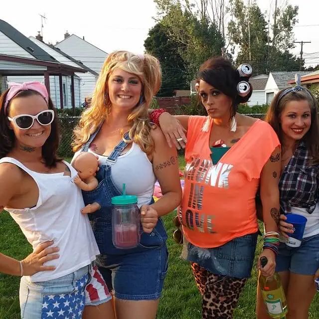 four girls are standing in the grass with their arms around each other and one is holding a water bottle