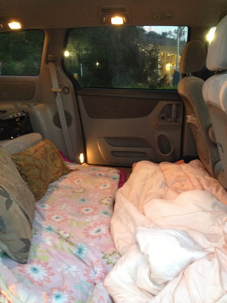 the inside of a van with blankets and pillows on it's bed, in front of two windows