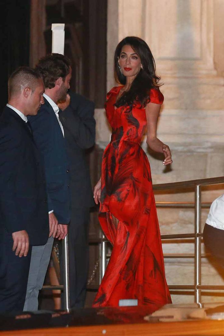 a woman in a long red dress is walking down the stairs while two men look on