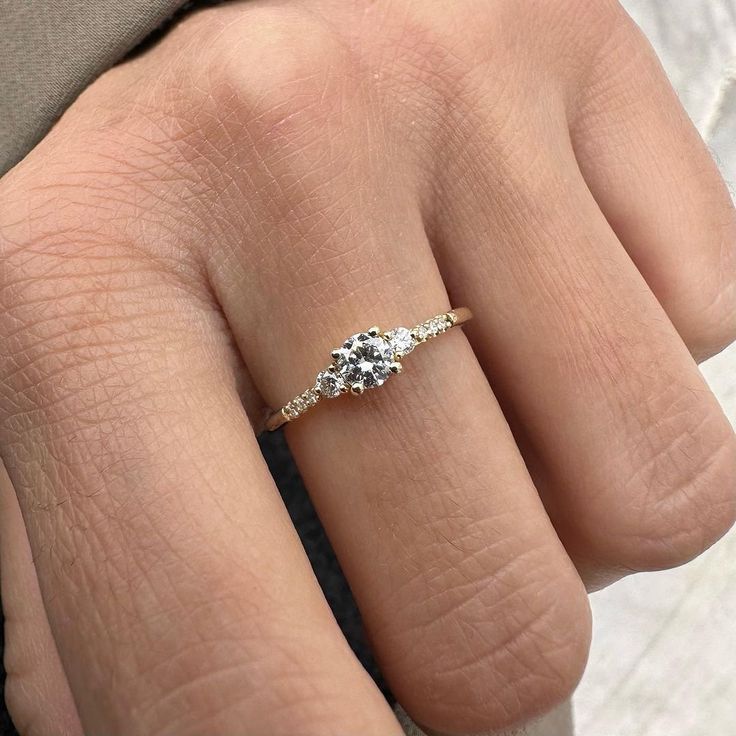 a woman's hand with a three stone ring on her left hand, and the other hand holding an engagement ring