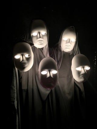 five mannequins with glowing eyes and heads in the dark, all wearing masks