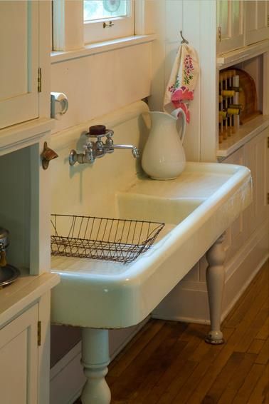 a white sink sitting under a window next to a wooden floor in a room with hardwood floors