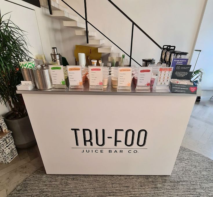 a counter with lots of products on it in front of a stair case that reads tru - foo juice bar co