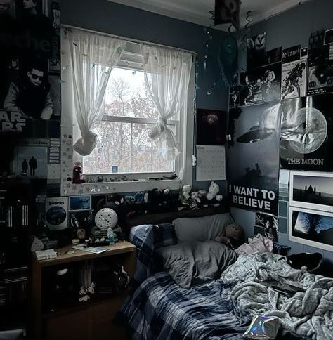 an unmade bed in a messy room with posters on the wall and windows above it