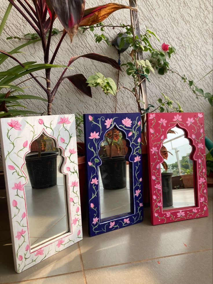 three small mirrors sitting on top of a table next to a plant and potted plant