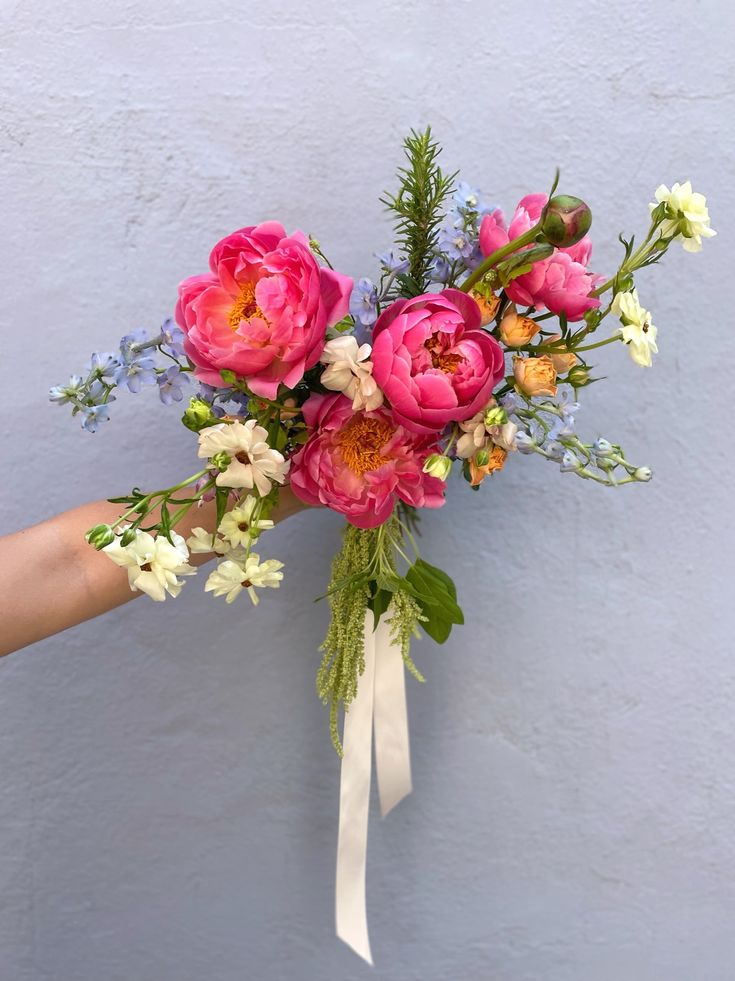 a bouquet of flowers is being held by a person's hand against a blue wall