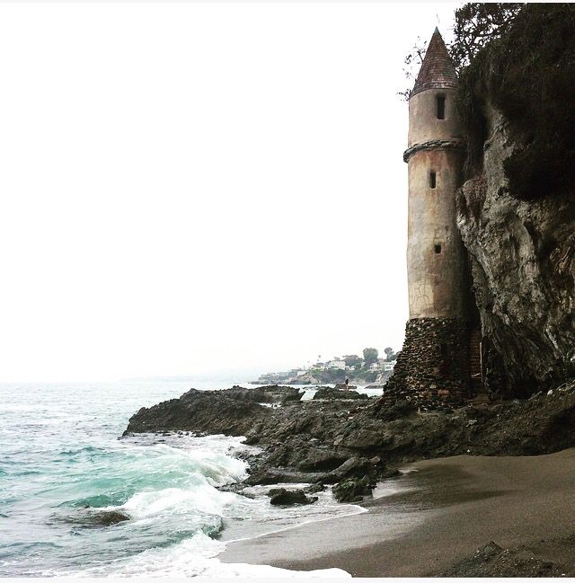 an old tower on the side of a cliff by the ocean with waves coming in