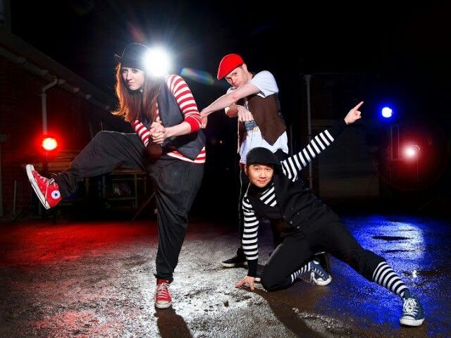 three people are posing for a photo in front of some lights and one person is holding his leg up