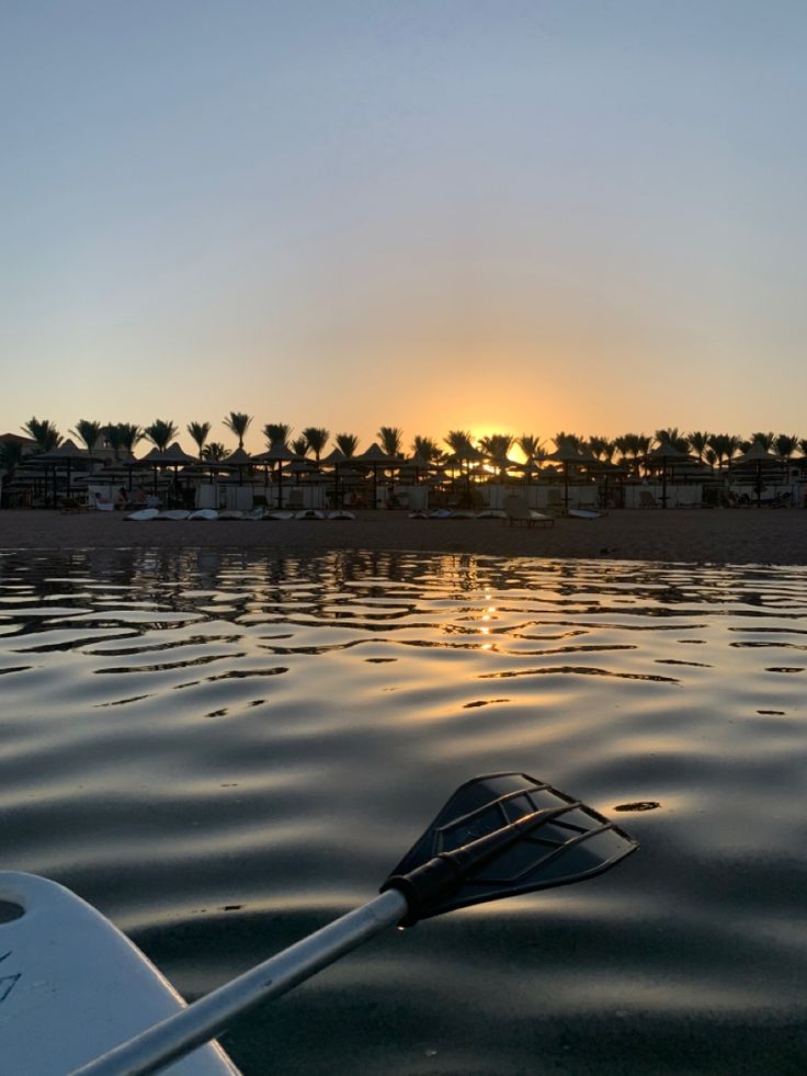 the sun is setting over the water with a paddle boat in it's foreground