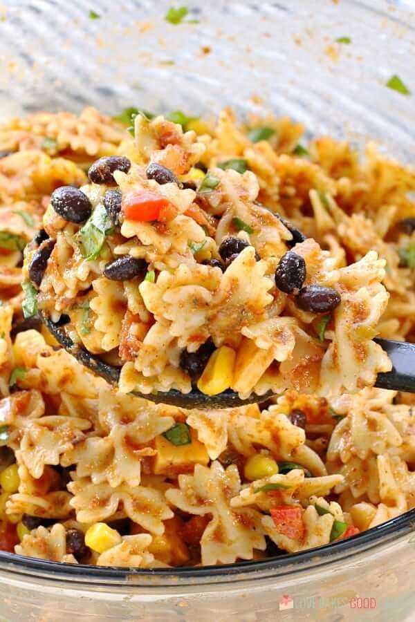 a glass bowl filled with pasta salad and a ladle full of the dish is ready to be eaten