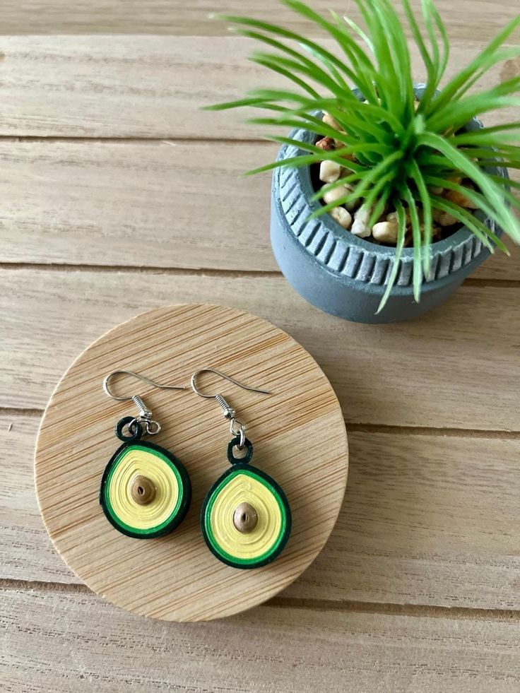 two green and yellow earrings sitting on top of a wooden table next to a potted plant