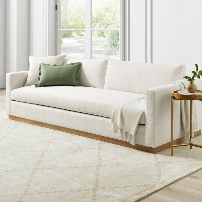 a living room with a white couch and green pillows on top of the rugs