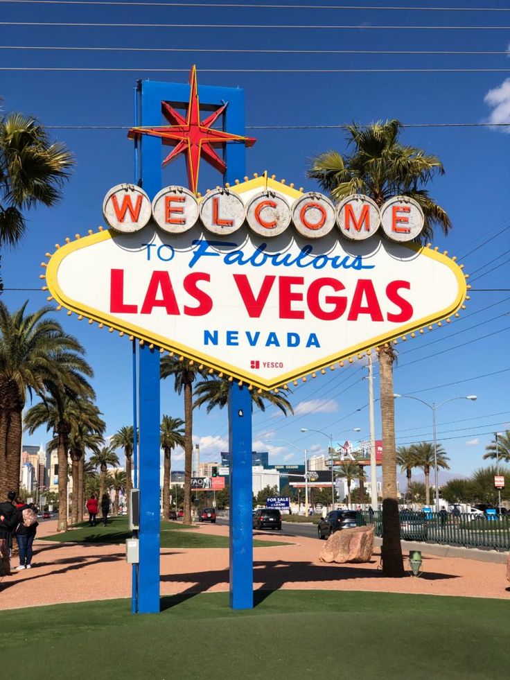 two people standing in front of the welcome sign to las vegas, nevada with their arms up