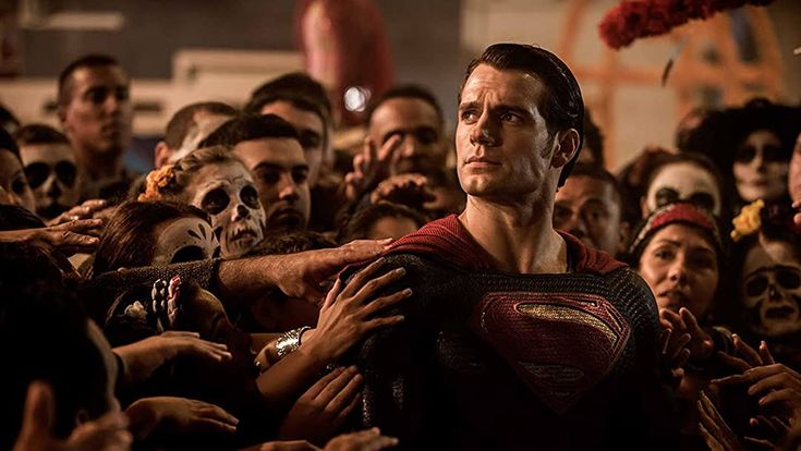 a man in a superman costume surrounded by other people and holding his hands out to him