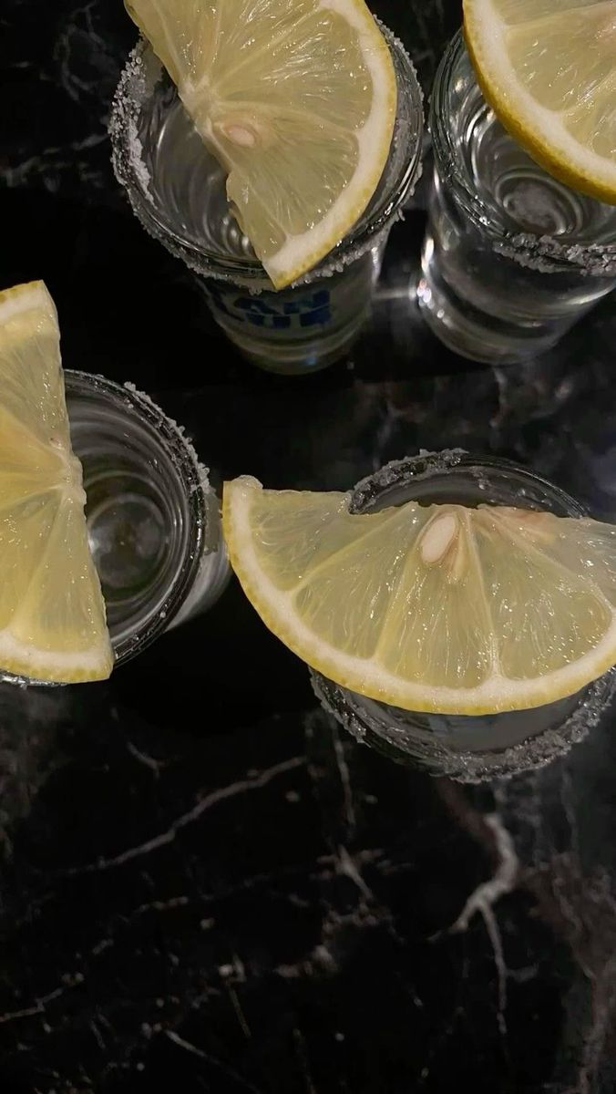 four glasses with lemon slices in them sitting on a black marble counter top next to each other