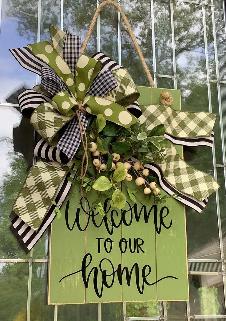 a welcome to our home sign hanging on the front door with green and white ribbon