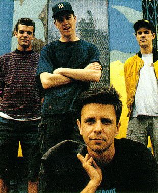 four young men posing for a photo in front of a wall with graffiti on it