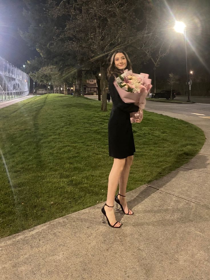 a woman standing on a sidewalk holding flowers