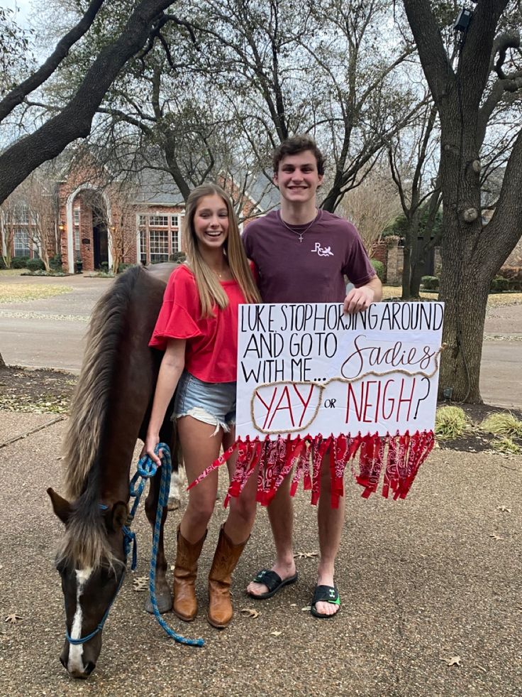 two people standing next to a horse holding a sign