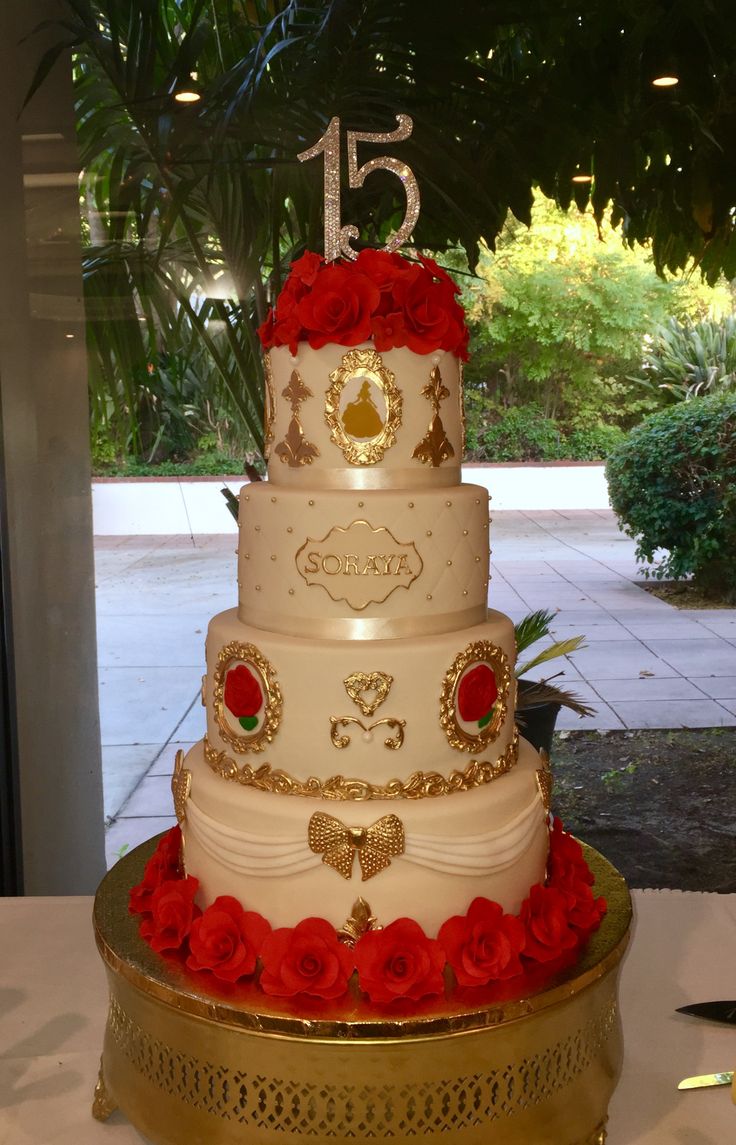 a three tiered wedding cake with red roses on the bottom and gold trimmings