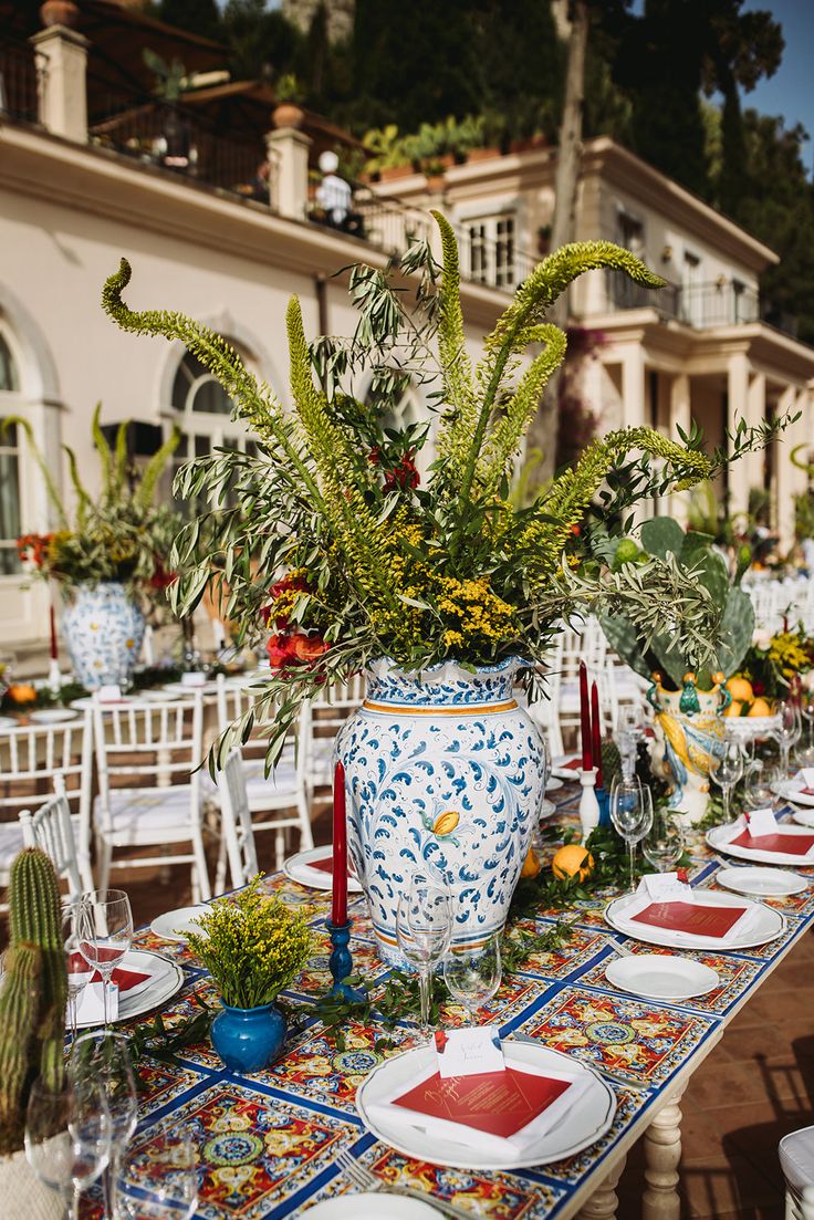 a table set up with plates and place settings for an outdoor dinner in front of a house