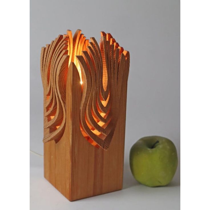 an apple sitting next to a wooden sculpture with lights on it's sides and a green apple in the background