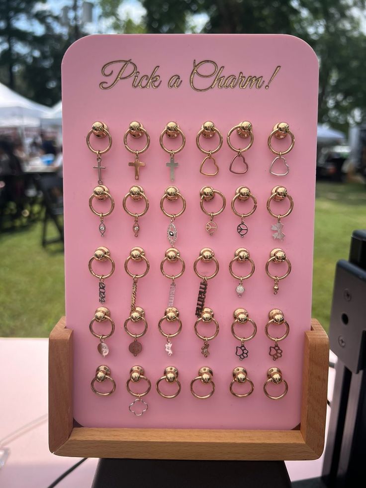 This unique display combines functionality with a chic aesthetic, making it the perfect addition to your permanent jewelry setup! Dimensions (without any base): 30 CHARM DISPLAY = approx. 6" x 8" 50 CHARM DISPLAY = approx. 8" x 8" 100 CHARM DISPLAY = approx. 10" x 11.75" --- PLEASE NOTE: Wooden stands are NOT offered with 100 charm displays! ---- Now featuring a sturdy wooden base and adorned with strategically placed rivets, adding an edgy yet refined flair. The rivets not only serve as eye-cat Charm Display Ideas, Charm Bar Display, Jewelry Pop Up Shop Display Ideas, Permanent Jewelry Display, Anthropologie Jewelry Display, Jewelry Vendor Display, Jewelry Display Ideas, Charm Display, Creative Jewelry Displays